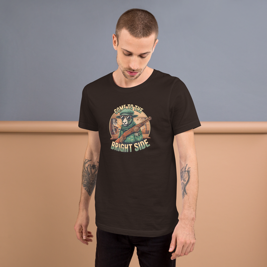 Mann trägt Unisex T-Shirt mit Schaf das Shotgun hält und Come to the Bright Side Schriftzug