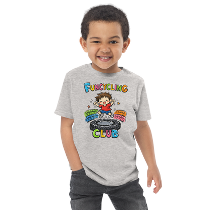Ein Junge trägt ein graues T-Shirt mit buntem "Funcycling Club" Print und einem Jungen der auf einem Reifen Trampolin springt
