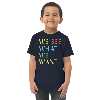 Junge trägt navy T-Shirt mit buntem We See What We Want Schriftzug